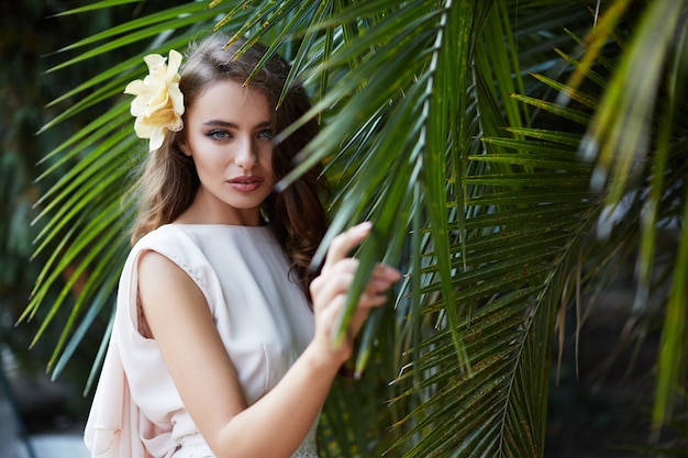 Attraente sposa con lunghi capelli ricci in abito da sposa a foglie verdi, foto del matrimonio, ritratto.