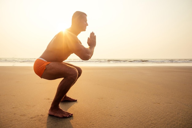 Attraente uomo a torso nudo durante l'allenamento in spiaggia. modello maschile sportivo facendo allenamento fitness su una spiaggia in una serata soleggiata al tramonto.