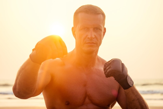 Attraente uomo a torso nudo durante l'allenamento su un modello maschile sportivo da spiaggia che fa allenamento fitness su una spiaggia in una soleggiata serata al tramonto