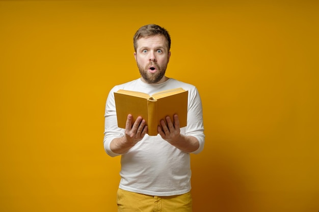 Attraente uomo barbuto con un libro in mano, affascinato da ciò che legge e guarda sorpreso