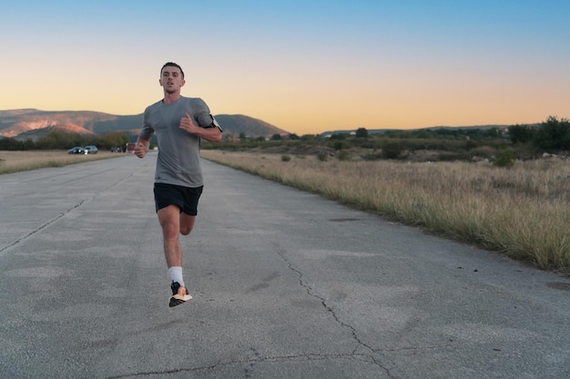 Attraente uomo in forma che corre veloce lungo la strada di campagna alla luce del tramonto, facendo jogging allenamento all'aperto. Foto di alta qualità