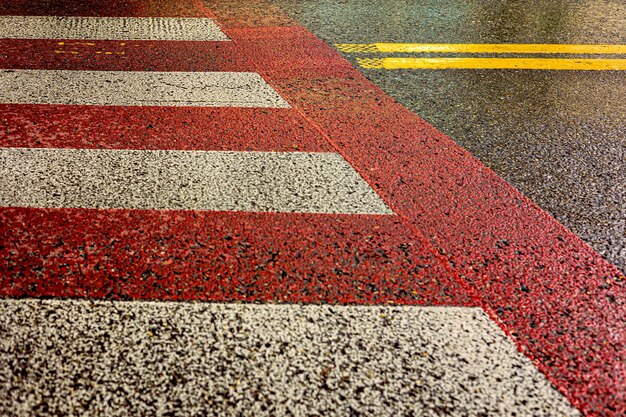 Attraversamento pedonale rosso e bianco e striscia divisoria gialla su pavimentazione bagnata
