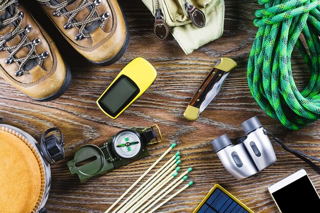 Attrezzatura da trekking con stivali, bussola, binocolo, fiammiferi, borsa da viaggio su fondo in legno. Concetto di stile di vita attivo.