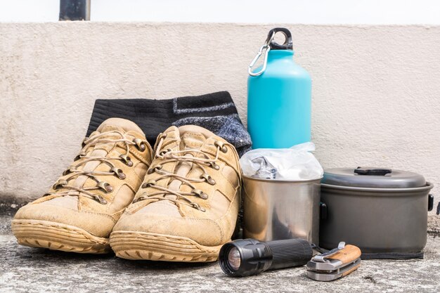 Attrezzatura da trekking o da trekking: scarponi, calze, coltello pieghevole, fornello a gas, borraccia, bollitore e torcia. Concetto di attività all'aperto. Still Life close up foto d'archivio.