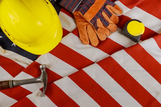 Attrezzatura di strumenti del casco giallo della costruzione di festa del lavoro per la festa federale felice del lavoro sopra sopra la bandiera americana.