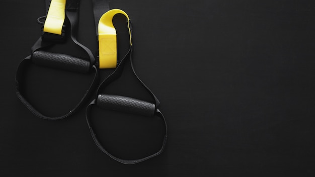 Attrezzatura per l'allenamento funzionale con cinturino nero e giallo su sfondo grigio. Accessori sportivi. Articoli per l'allenamento fitness e palestra per un sano. Banner TRX