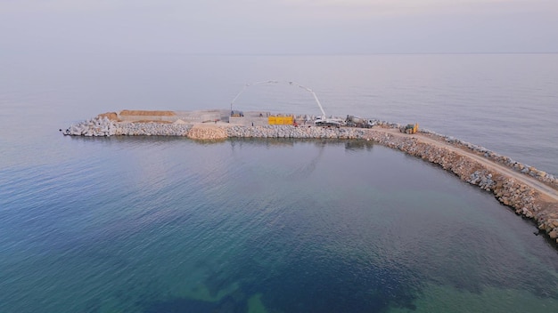 Attrezzature per l'edilizia pesante stanno costruendo un frangiflutti Colata di cemento su un molo in costruzione nel mare