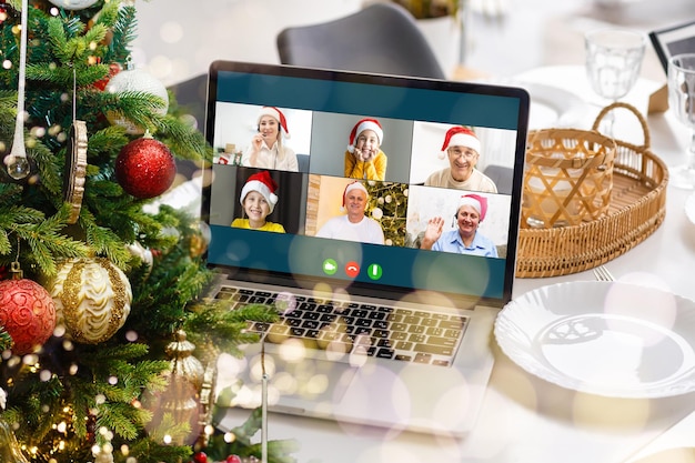 Auguri di Natale online. una donna con un maglione bianco e un cappello rosso da Babbo Natale utilizza un laptop per effettuare videochiamate ad amici, genitori e per lo shopping online.