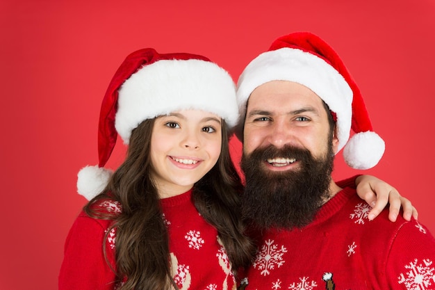 Auguri. felice padre e figlia amano il natale. piccola ragazza e cappello di babbo natale. papà e bambino sfondo rosso. periodo natalizio. festa di fine anno. felice di stare insieme. vacanza invernale con la famiglia.