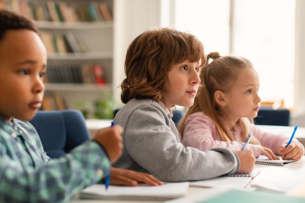 Aula elementare di diversi bambini che ascoltano attentamente il loro insegnante che scrive durante l'esercizio