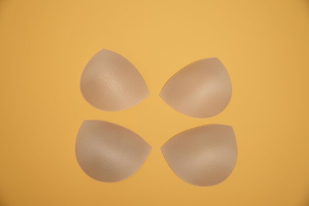 Aumenta le dimensioni del seno. Imbottiture per reggiseno e reggiseno color crema isolato su sfondo arancione