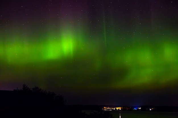 Aurora boreale sopra la città sulla costa. Luci polari nel cielo stellato notturno sul lago.