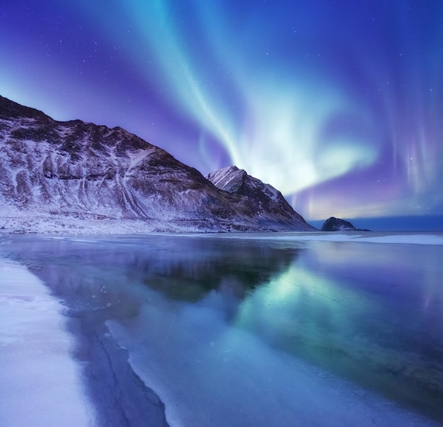 Aurora borealis sulle isole Lofoten Norvegia Luci settentrionali verdi sopra le montagne Paesaggio invernale notturno con aurora e riflesso sulla superficie dell'acqua Norvegiaimmagine