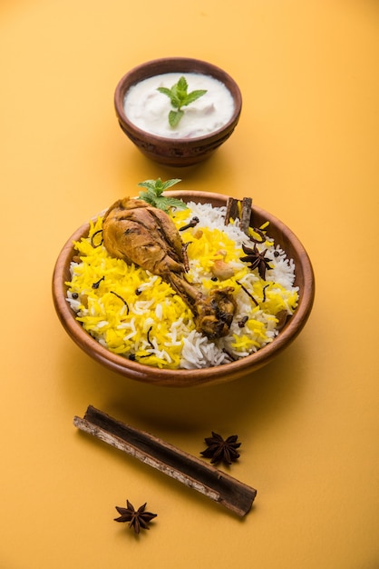Autentico pollo Biryani servito in una ciotola o in un piatto su sfondo colorato o in legno. È una deliziosa ricetta di riso basmati mescolato con pollo marinato piccante servito con insalata. Messa a fuoco selettiva