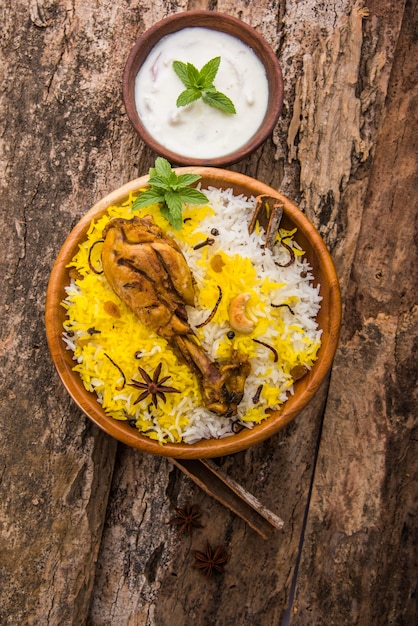 Autentico pollo Biryani servito in una ciotola o in un piatto su sfondo colorato o in legno. È una deliziosa ricetta di riso basmati mescolato con pollo marinato piccante servito con insalata. Messa a fuoco selettiva