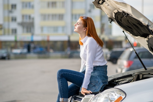 Autista della donna sollecitato giovani vicino all'automobile rotta con assistenza aspettante del cappuccio schioccato.