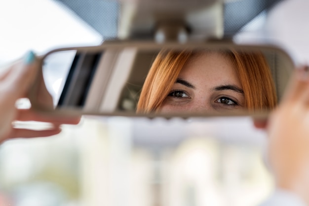 Autista della giovane donna che controlla lo specchio di retrovisione che guarda indietro mentre guidando un'automobile.