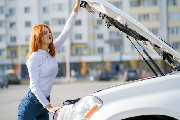 Autista della giovane donna che sta vicino all'automobile rotta con il cappuccio aperto.