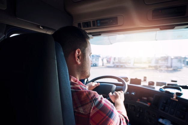 Autista di camion di mezza età professionista in abiti casual alla guida di un camion per un lungo percorso di trasporto che consegna merci al mercato.