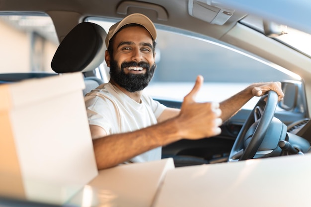 Autista di fattorino indiano che gesturing i pollici in su seduto in macchina