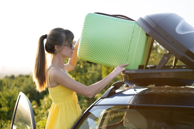 Autista di giovane donna che mette la valigia verde all'interno del portapacchi per auto Concetto di viaggio e vacanze