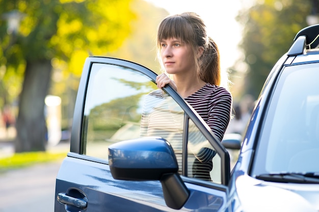 Autista di giovane donna che si gode una calda giornata estiva in piedi accanto alla sua auto sulla strada della città. Concetto di viaggio e vacanza.
