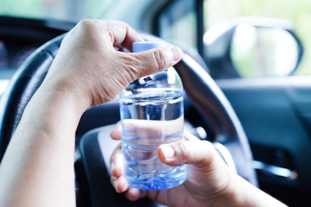 Autista donna asiatica tenere acqua fredda per bere in macchina pericolosa e rischiare un incidente