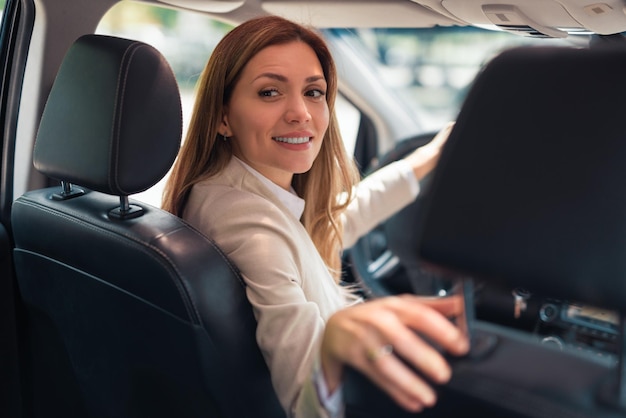 Autista felice della donna di affari che si siede in automobile che tiene al volante