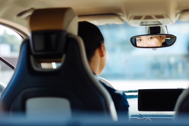 Autista professionista. Bella donna piacevole che guarda nello specchietto retrovisore mentre è seduto al volante