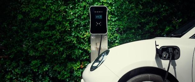 Auto EV progressiva con vista laterale con sfondo verde fogliame della stazione di ricarica