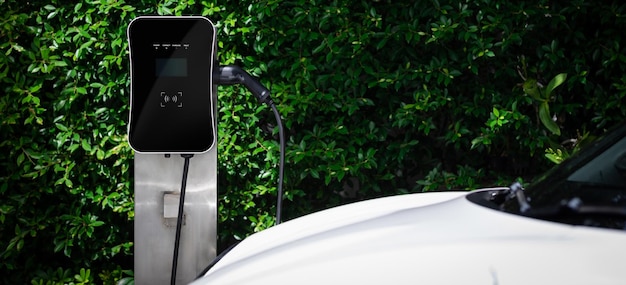 Auto EV progressiva con vista laterale con sfondo verde fogliame della stazione di ricarica