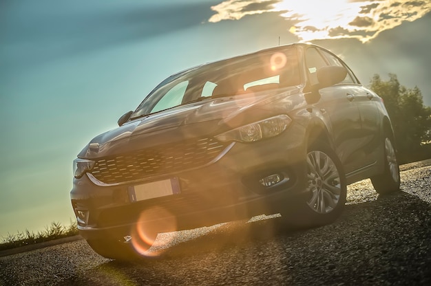 Auto moderna ripresa dal basso con grandangolo dietro con tramonto e una bella luce che contrasta. Chiarore di luce sull'obiettivo.