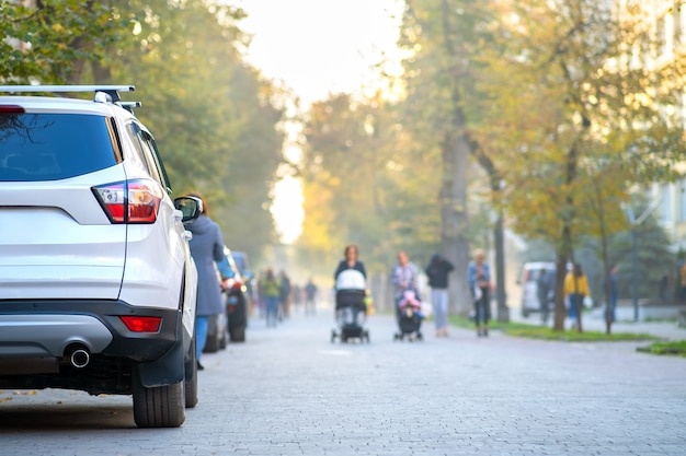 Auto parcheggiata sul lato di una strada cittadina in una luminosa giornata autunnale con persone sfocate che camminano nella zona pedonale