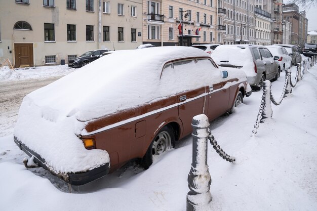 Auto parcheggiate coperte di neve su una strada innevata non pulita dopo la nevicata. Maltempo invernale, aumento delle precipitazioni e concetto di livelli di neve.