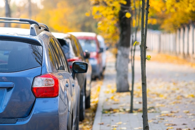 Auto parcheggiate in fila su un lato di una strada cittadina in una luminosa giornata autunnale.