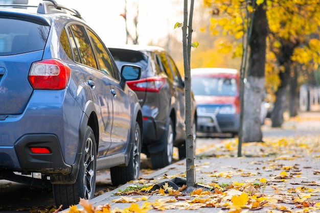 Auto parcheggiate in fila su un lato di una strada cittadina in una luminosa giornata autunnale.