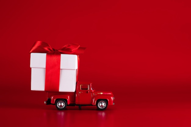 Auto rossa con una confezione regalo su sfondo rosso. Concetto - consegna di regali per le vacanze, San Valentino, Giornata internazionale della donna, 14 febbraio, 8 marzo. Shopping, vendita.