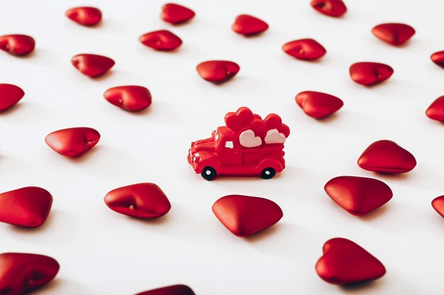 Auto rossa in miniatura e molti cuori su sfondo bianco Concetto di San Valentino