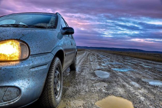 Auto sporca su una strada fangosa contro un cielo nuvoloso durante l'alba