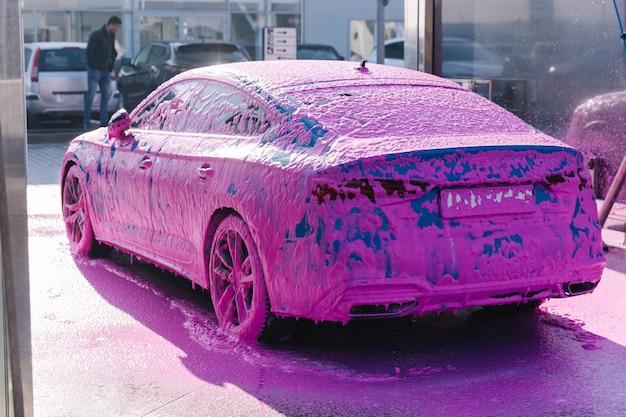 Auto sportiva di lusso blu su auto self service lavaggio schiuma rosa su vista posteriore automatica