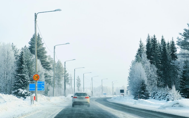 Auto su strada invernale con neve in Finlandia. Auto e paesaggio freddo della Lapponia. Automobile sulla foresta d'Europa. Giro in autostrada della città finlandese. Carreggiata e percorso innevato viaggio su strada. Guida