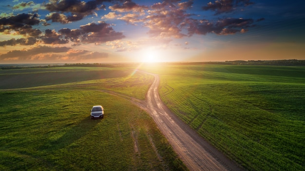 Auto su una strada sterrata in un campo di girasoli e grano con la luce del sole