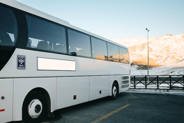 Autobus bianco parcheggiato contro le montagne innevate sullo sfondo cartellone pubblicitario bianco vuoto