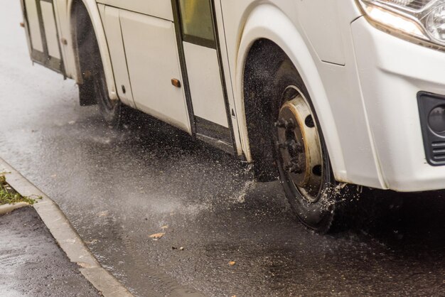 Autobus municipale bianco che si muove su strada piovosa con schizzi d'acqua