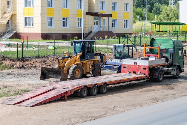 Autocarro con pianale ribassato, rullo compressore e trattore gommato in riparazione su strada