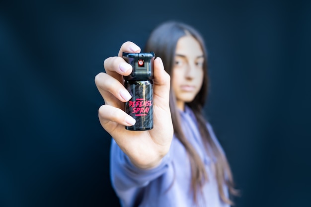 Autodifesa di una giovane ragazza adolescente con spray al peperoncino. Isolato su sfondo scuro.