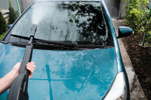 Autolavaggio a casa da solo. Primo piano ad alta pressione dell'autolavaggio. Un uomo lava un'auto verde.