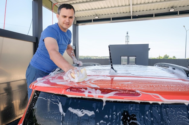 Autolavaggio manuale Un uomo con acqua saponata lava la sua auto Concetto di pulizia