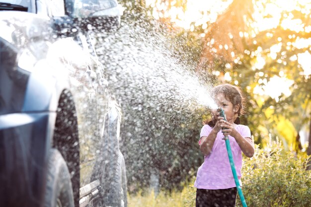 Automobile asiatica felice di lavaggio del genitore di aiuto della ragazza del bambino sull&#39;acqua che spruzza con luce solare