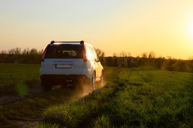 Automobile bianca del suv alla strada del campo sul tramonto